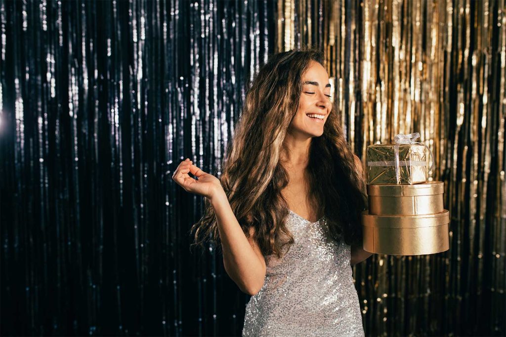 Woman in the studio holding some wrapped prizes in front of a sparkling background